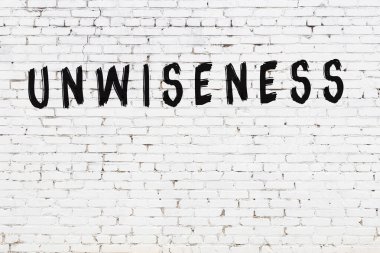 Beyaz tuğla duvarda siyah boyayla yazılmış akılsızlık..