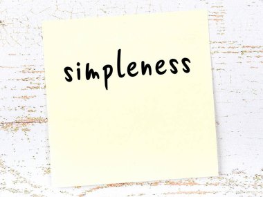 Basitlik hakkında hatırlatma kavramı. Tahta duvarda üzerinde yazı olan sarı yapışkan kağıt.