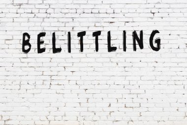 Yazı, beyaz tuğla duvara siyah boyayla yazılmış aşağılama..