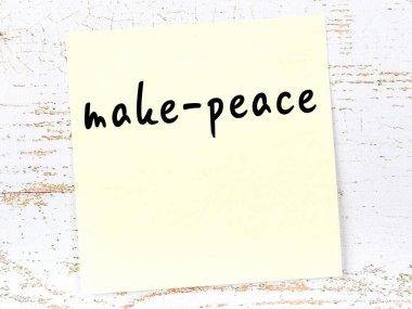 Tahta duvardaki sarı yapışkan notta el yazısıyla yazılmış barış yazısı var.