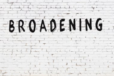 Üzerinde yazı olan beyaz tuğla duvar siyah boyayla el yazısıyla genişletiliyor.