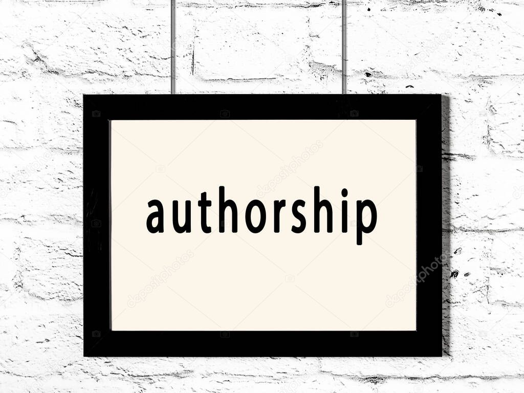 Black wooden frame with inscription authorship hanging on white brick wall 