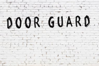 Beyaz tuğlalı duvar. Kapıda yazı var. Siyah boyayla yazılmış.