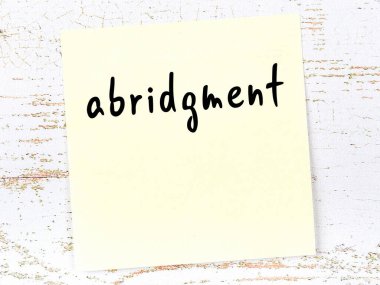 Tahta duvarda el yazısıyla yazılmış kısaltmalı sarı yapışkan not.