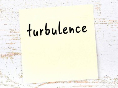 Tahta duvarda el yazısı türbülans olan sarı yapışkan bir not.