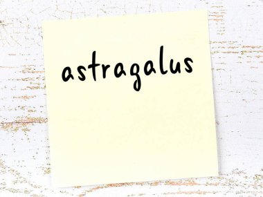 Tahta duvardaki sarı yapışkan notta el yazısı astragalus yazıyor.