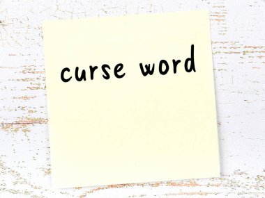 Tahta duvardaki sarı yapışkan notta el yazısıyla yazılmış lanet kelimesi var.