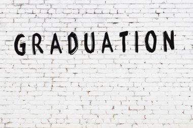 Mezuniyet töreninde siyah boyayla yazılmış beyaz tuğlalı bir duvar.