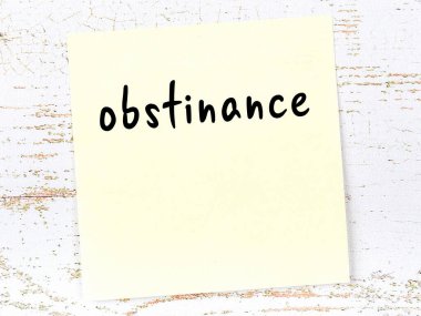 Tahta duvardaki sarı yapışkan notta el yazısıyla yazılmış inat var.