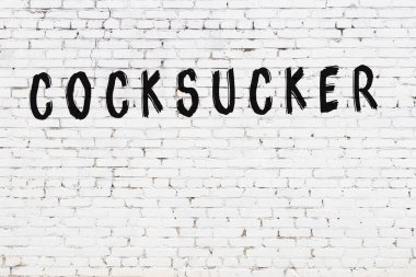 White brick wall with inscription cocksucker handwritten with black paint