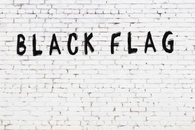 Üzerinde siyah boya yazılı siyah bayrak olan beyaz tuğla bir duvar.