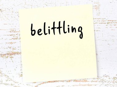 Tahta duvardaki sarı yapışkan notta el yazısıyla yazılmış aşağılayıcı bir yazı var.