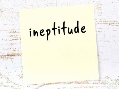 Tahta duvardaki sarı yapışkan notta el yazısıyla yazılmış beceriksizlik var.