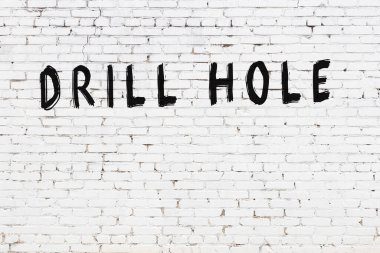 Üzerinde siyah boya ile el yazısıyla matkap deliği olan beyaz tuğla bir duvar.