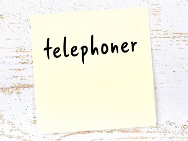 Ahşap duvardaki sarı yapışkan notta el yazısıyla yazılmış telefon var.