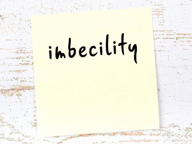 Ahşap duvardaki sarı yapışkan notta elle yazılmış embesillik yazılıydı.