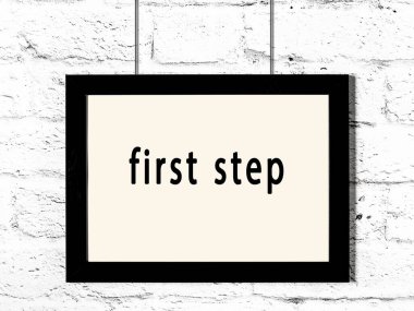 Üzerinde yazı olan siyah ahşap çerçeve beyaz tuğla duvara asılı ilk adım 