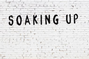 Yazı, beyaz tuğla duvara siyah boya ile yazılmış..