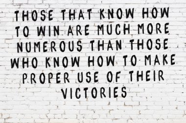 Beyaz tuğla duvara zekice alıntılar yazılı siyah bir yazı.