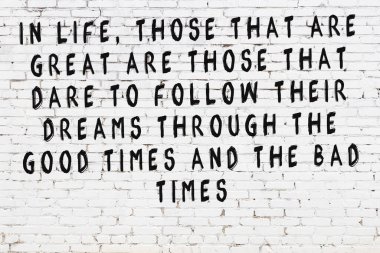 Beyaz tuğla duvara zekice alıntılar yazılı siyah bir yazı.