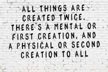 Beyaz tuğla duvara zekice alıntılar yazılı siyah bir yazı.