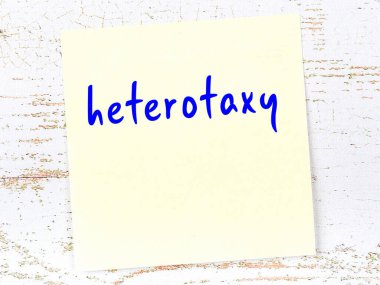 Concept of reminder about heterotaxy. Yellow sticky sheet of paper on wooden wall with inscription