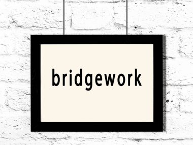 Black wooden frame with inscription bridgework hanging on white brick wall 