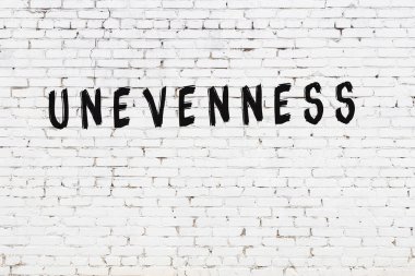 Beyaz tuğlalı duvara siyah boya ile yazılmış bir yazı düzensizliği.