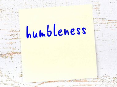 Tahta duvardaki sarı yapışkan notta el yazısıyla yazılmış alçakgönüllülük yazısı var.