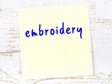 Nakışla ilgili bir hatırlatma. Tahta duvarda üzerinde yazı olan sarı yapışkan kağıt.