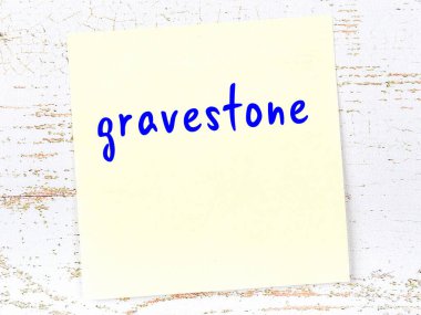 Tahta duvardaki sarı yapışkan notta el yazısıyla yazılmış mezar taşı var.