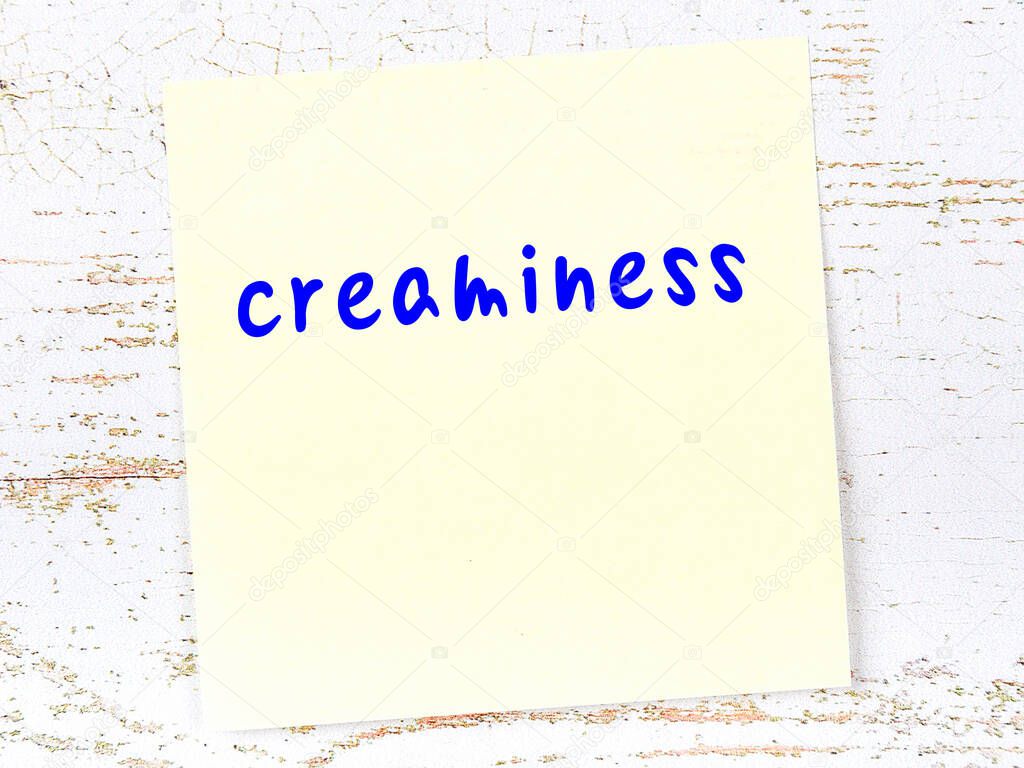 Concept of reminder about creaminess. Yellow sticky sheet of paper on wooden wall with inscription