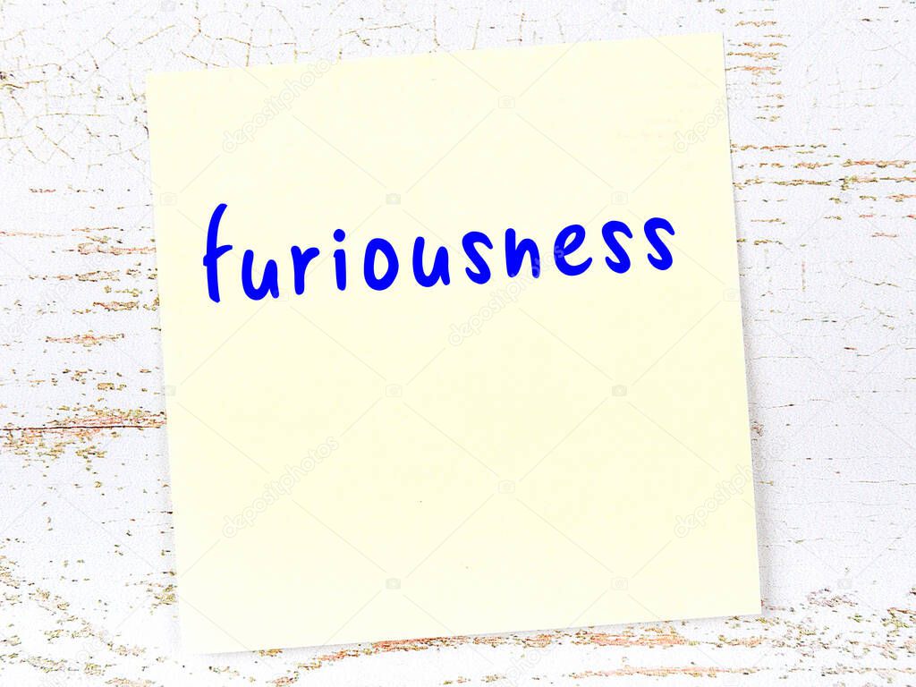 Yellow sticky note on wooden wall with handwritten inscription furiousness