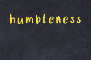 Tebeşir el yazısıyla yazılmış mütevazilik siyah masanın üzerinde.