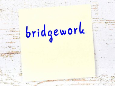 Tahta duvardaki sarı yapışkan notta el yazısıyla yazılmış köprü işi var.