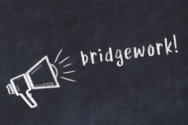 Hoparlörün tebeşir çizimi ve siyah masanın üzerine el yazısıyla yazılmış köprü çalışması