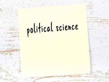 Tahta duvardaki sarı yapışkan notta el yazısıyla yazılmış politik bilimler var.
