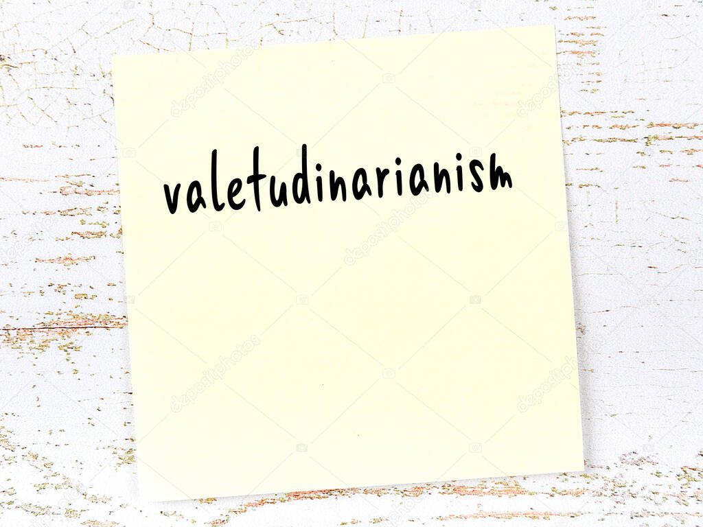 Yellow sticky note on wooden wall with handwritten inscription valetudinarianism