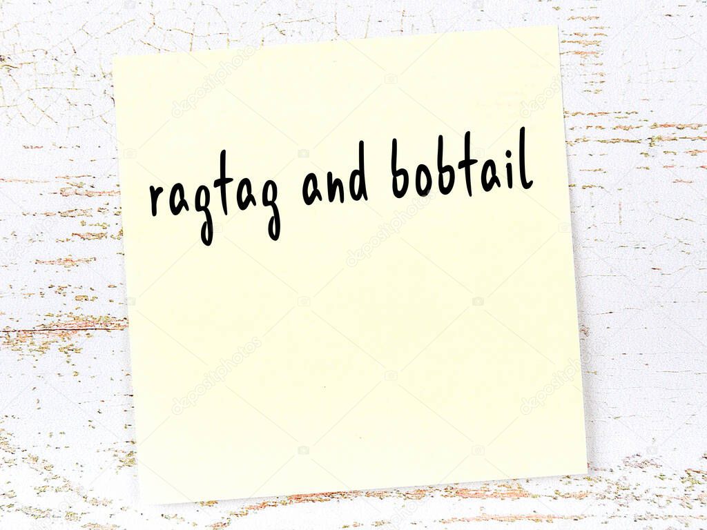 Concept of reminder about ragtag and bobtail. Yellow sticky sheet of paper on wooden wall with inscription