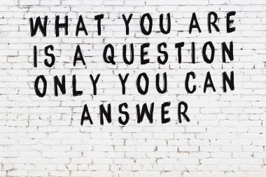 Beyaz tuğla duvara zekice alıntılar yazılı siyah bir yazı.