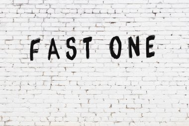 Üzerinde yazı olan beyaz tuğla bir duvar, hızlı biri siyah boyayla yazılmış.