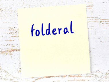 Tahta duvardaki sarı yapışkan notta el yazısıyla yazılmış klasör var.