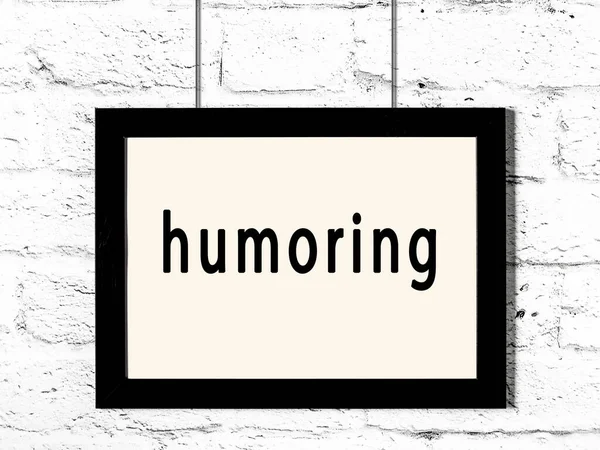 Μαύρο Ξύλινο Πλαίσιο Επιγραφή Humoring Κρέμεται Λευκό Τοίχο Τούβλο — Φωτογραφία Αρχείου