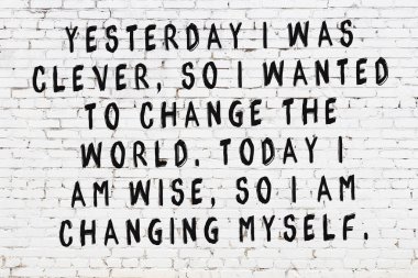 Beyaz tuğla duvara zekice alıntılar yazılı siyah bir yazı.