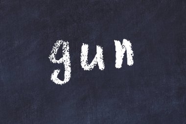 Tebeşir el yazısıyla yazılmış bir silah siyah masanın üzerinde.