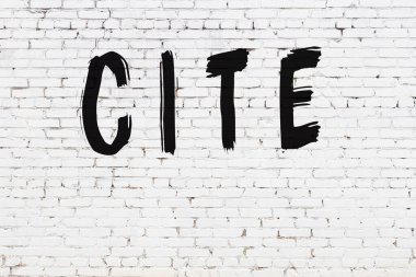 Üzerinde yazı olan beyaz tuğla duvar siyah boyayla el yazısıyla yazılmış.