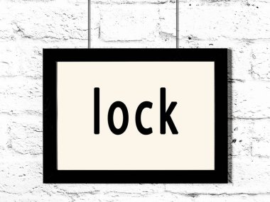 Siyah ahşap çerçeve, beyaz tuğla duvarda yazı kilidi asılı. 