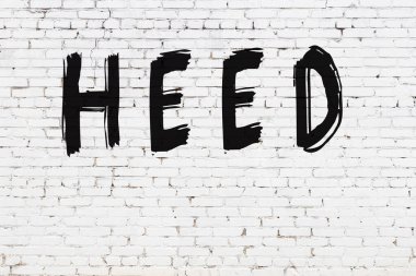 Yazı, beyaz tuğla duvara siyah boya ile yazılmış..