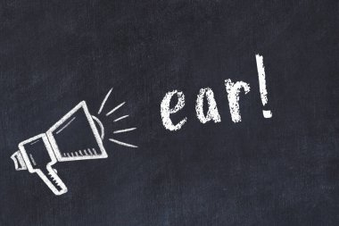 Hoparlörün tebeşir çizimi ve siyah masanın üzerine el yazısıyla yazılmış kulaklık.