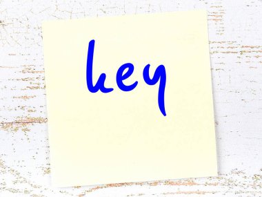 Tahta duvardaki sarı yapışkan notada el yazısıyla yazılmış anahtar var.